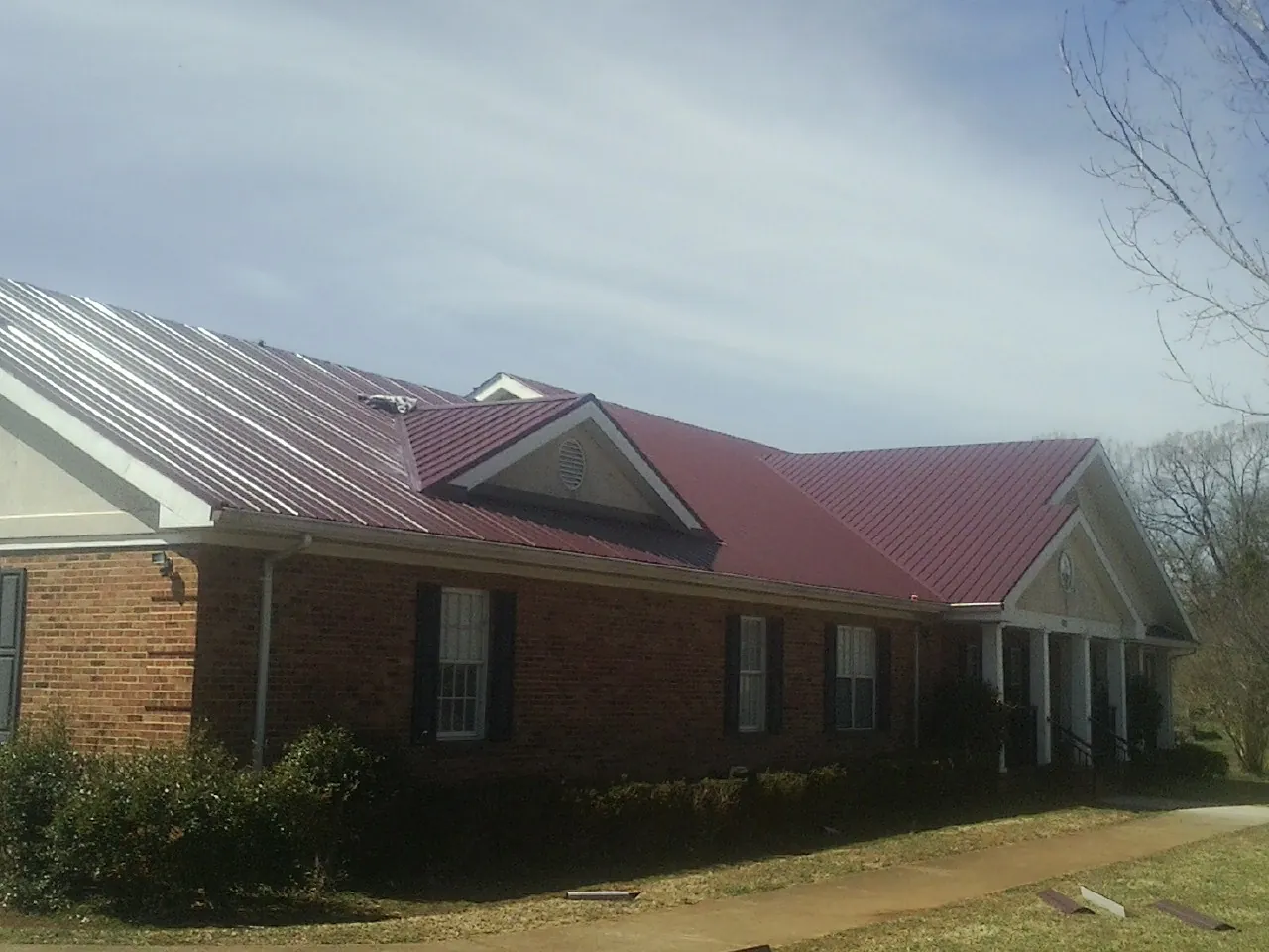 Red metal roof with gabled entries on a long brick building, from a Hail Damage Roof Repair job in Dickerson