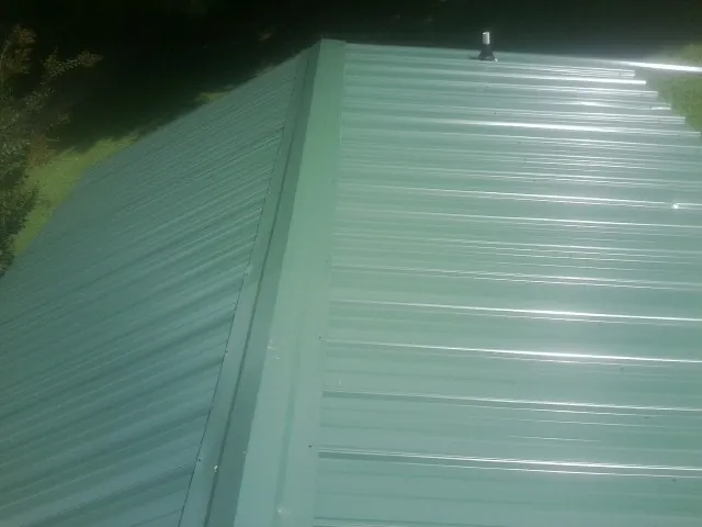 New green metal panels meeting at the ridge of a roof — Flat Roof Repair work by our crew in Dickerson