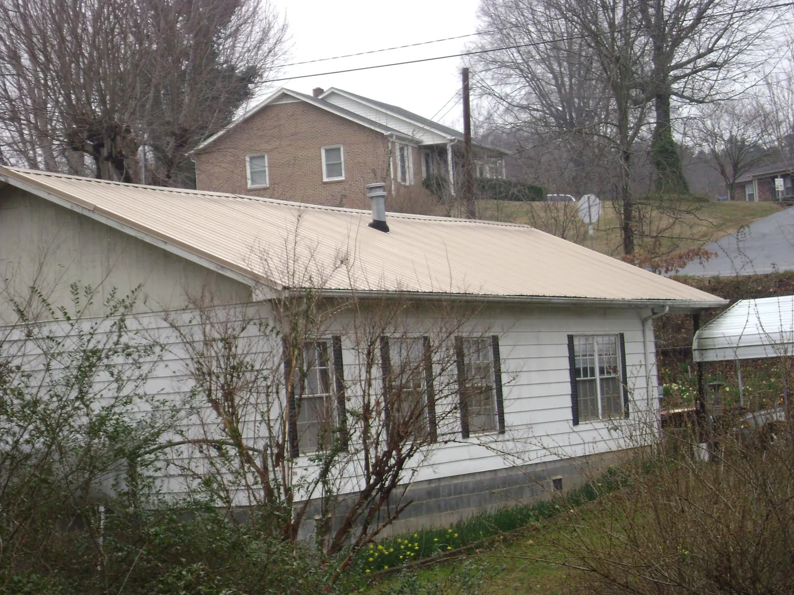 Tan metal roof on a white sided house set into a hillside — Commercial Roofing by Roofing Brothers in Dickerson